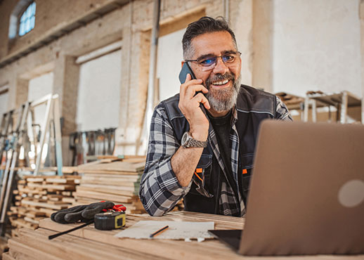 A man in his workshop using a laptop computer while on a phone