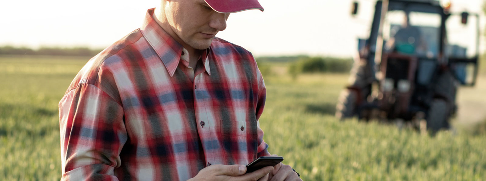 A farmer using his smartphone in a field with a tractor